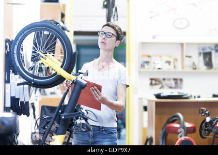 Woman in bicycle workshop holding clipboard checking bicycle Stock Photo