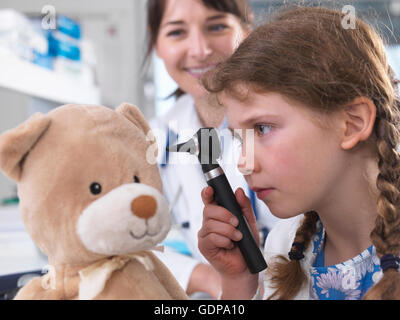 Girl using otoscope to examine teddy bear Stock Photo