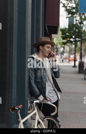 Young man leaning against wall, using smartphone Stock Photo