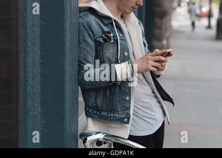 Young man leaning against wall, using smartphone, mid section Stock Photo