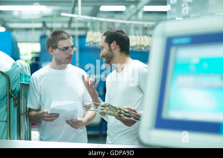 Man in launderette holding coat hangers talking to colleague Stock Photo