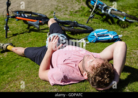 Cyclist lying down on grass by bicycle Stock Photo