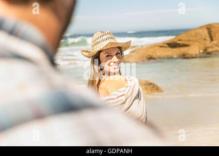 Over shoulder view of woman wrapped in blanket on beach, Cape Town, South Africa