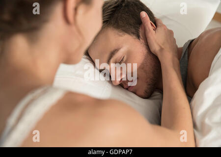 Young woman lying in bed touching sleeping boyfriends cheek Stock Photo