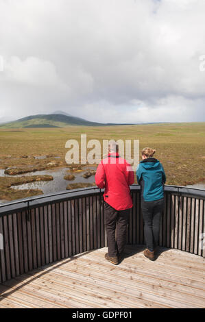 Young couple looking over peatland pools from the viewing tower on the RSPB Dubh Lochan Trail, Forsinard, Sutherland, Scotland.