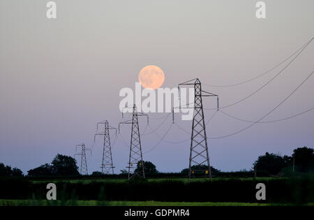 Full moon rising behind electricity pylons Stock Photo
