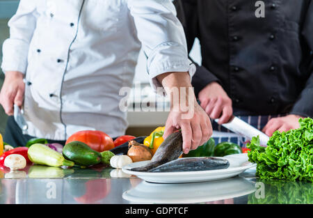 Chefs preparing food in teamwork at restaurant kitchen, cutting vegetables and fish Stock Photo