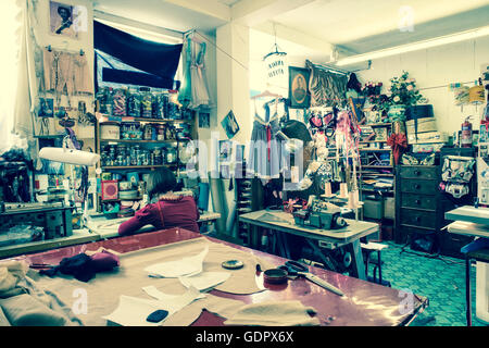 Inside a tailoring shop with a dressmaker with back turned working on a sewing machine. Stock Photo