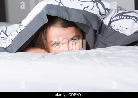 Child or teen under covers in bed Stock Photo