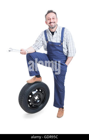 Cheerful mechanic with tools posing close to auto tire on overalls isolated on whitebackground Stock Photo