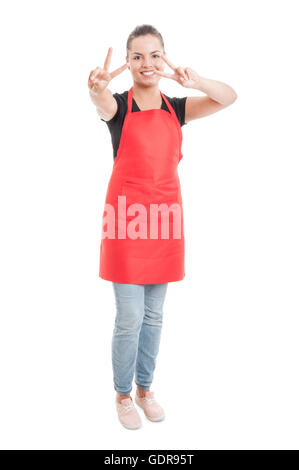 Young hypermarket saleswoman in red apron doing double peace gesture isolated on white studio background Stock Photo