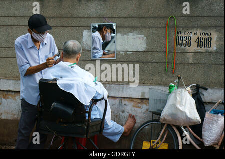 Traditional lifestyle of poor people in Asia urban, Vietnamese male barber work at open air shop on pavement Stock Photo