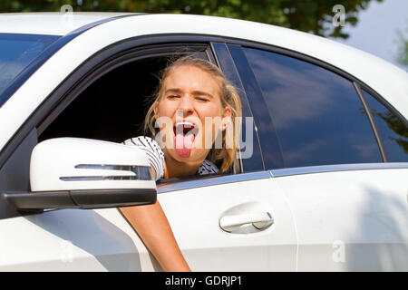 Young woman sitting in a car and sticking tongue out Stock Photo