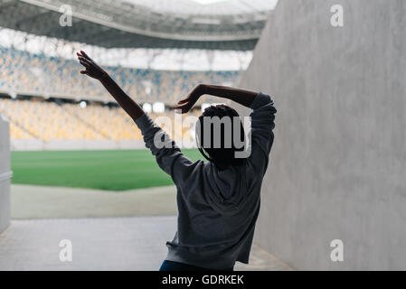 Young attractive african american female in gray hoodie dancing alone at empty stadium Stock Photo