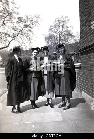 1960s, historical, four young female graduates in academic dress wearing robes and mortarboards stand together on a pavement outside after a University degree presentation, England. Stock Photo