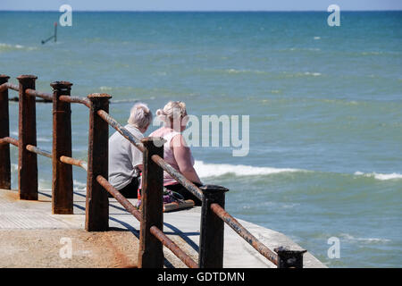 Two people sat on sea wall looking out to sea Stock Photo