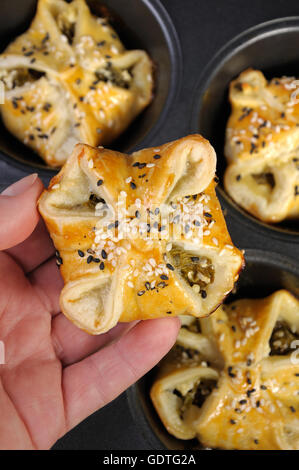 bun puff pastry with spinach and ricotta in a hand on a background of trays  baking Stock Photo