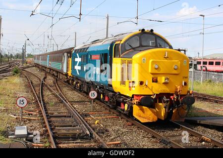 Class 37 diesel-electric locomotive in British rail large logo livery approaching Carnforth station with a passenger train. Stock Photo