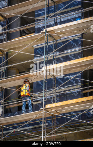 Construction worker in bright safety vest standing on scaffolding of tall office building under construction Stock Photo