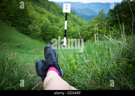 Legs of woman hiker sitting on top of a high mountain above a green forest. Freedom concept Stock Photo