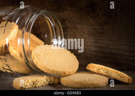 Homemade butter biscuits spilling from a glass jar on a wooden table. Stock Photo