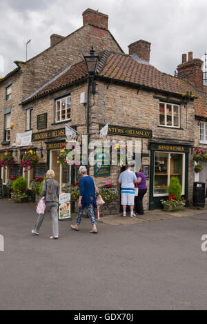 2 people pass while a couple buy ice creams at Hunters of Helmsley, an independent delicatessen - Helmsley, North Yorkshire, GB. Stock Photo