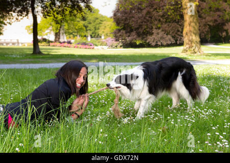 Laughing young woman trying to win at rope pulling with her border collie dog Stock Photo