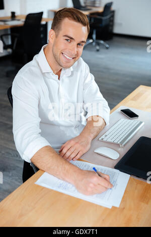 Cheerful young businessman writing at the table on workplace Stock Photo