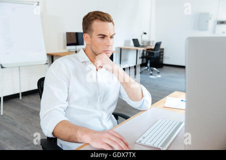Thoughtful young businessman thinking and using computer at work Stock Photo