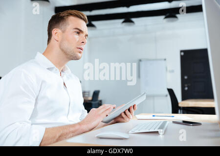 Serious young businessman using tablet and computer in office Stock Photo