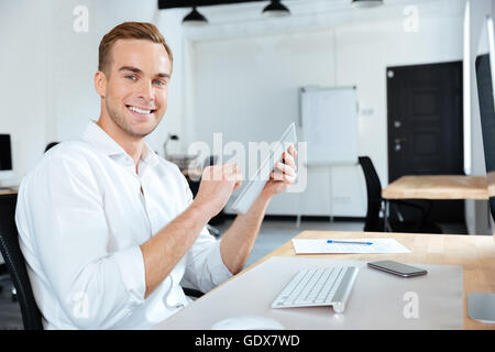 Cheerful young businessman smiling and using tablet at the table Stock Photo