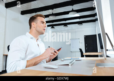 Concentrated young businessman using computer and mobile phone at workplace Stock Photo