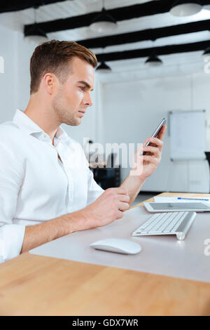 Serious young businessman sitting at workplace and using cell phone Stock Photo