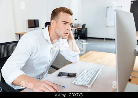 Thoughtful young businessman thinking and using computer in office Stock Photo