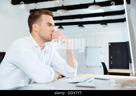 Pensive young businesman working with computer and thinking at workplace Stock Photo