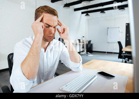 Stressed young businessman touching his temples and having a headache in office Stock Photo