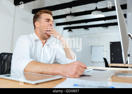 Sleepy tired young businessman working and yawning in office Stock Photo