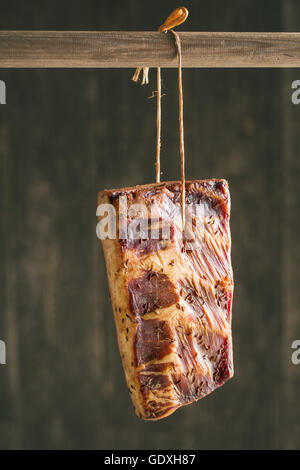 Fresh smoked bacon hanging on wooden stick. Stock Photo