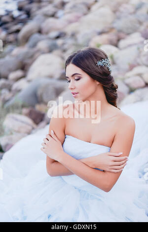 Gorgeous brunette European type sits in profile on the beach, looking romantically into the distance. Beautiful hair decoration handmade Stock Photo