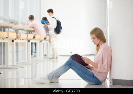 Side view of young female college student sitting and reading and looking down with three college students at library Stock Photo