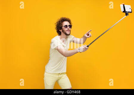 Stylish curly-haired man taking selfie with monopod Stock Photo