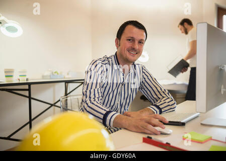 Architect working on computer and smiling in office, Bavaria, Germany Stock Photo