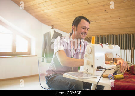 Male dressmaker stitching cloth on sewing machine, Bavaria, Germany Stock Photo