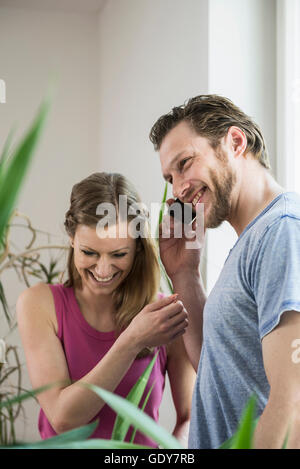 Mid adult man talking on mobile phone in living room and smiling, Munich, Bavaria, Germany Stock Photo