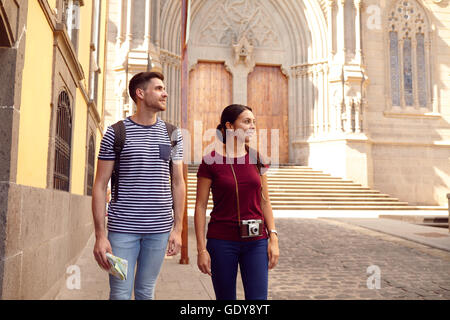Young tourist couple on vacation with a backpack and map looking sideways while walking dressed casually in jeans and t-shirts w Stock Photo