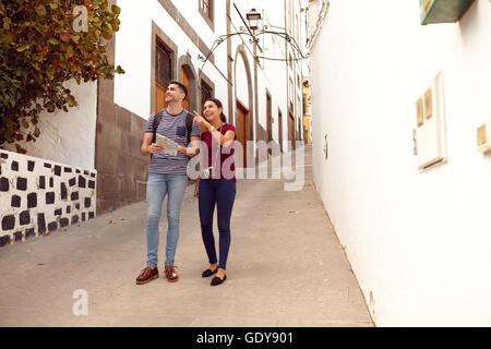 Young tourist couple on vacation with a backpack and map walking down a narrow street and pointing while dressed casually in jea Stock Photo