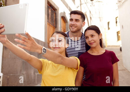 Cute tourist couple on vacation with a backpack taking selfies with a new friend in a narrow street while dressed in casual clot Stock Photo
