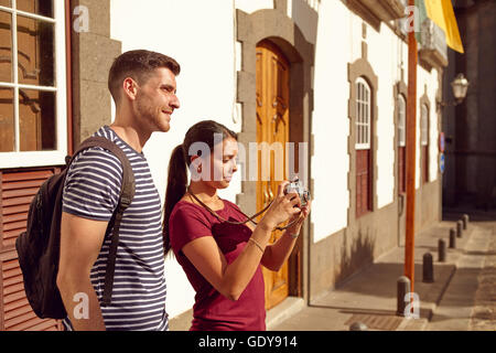 Young tourist couple on vacation with a backpack taking a picture in a narrow street while dressed in casual clothes Stock Photo
