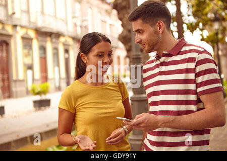 Young couple looking at each other and talking with a cell phone and making hand signs while dressed casually in jeans and t-shi Stock Photo