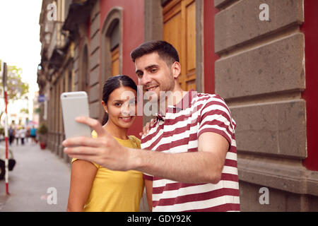 Young couple looking at cell phone with toothy smiles to take a selfie, dressed casually in t-shirts with old buildings behind t Stock Photo